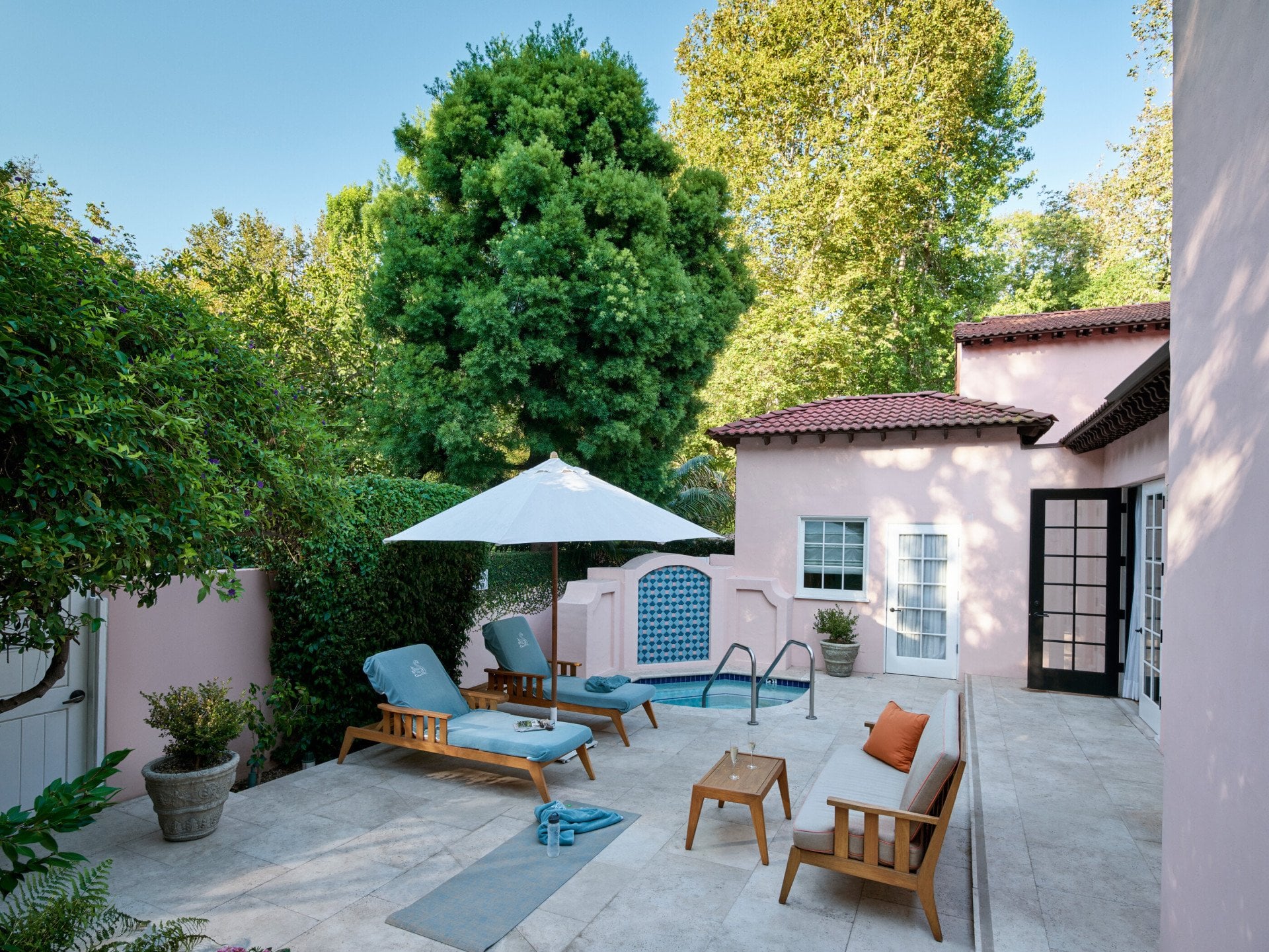 Full view of the patio in the legendary Chalon Suite with outdoor jacuzzi, two lounge chairs with an umbrella covering them, and a small side table with two glasses of champagne on top.
