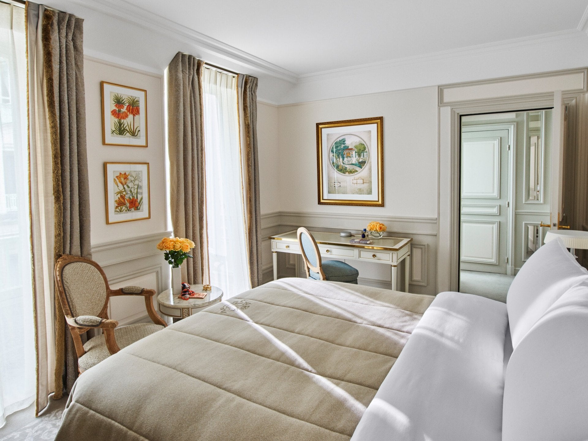 Bedroom in beige and white shades, with queen bed, white wood desk and armchair, at Le Meurice, Paris.