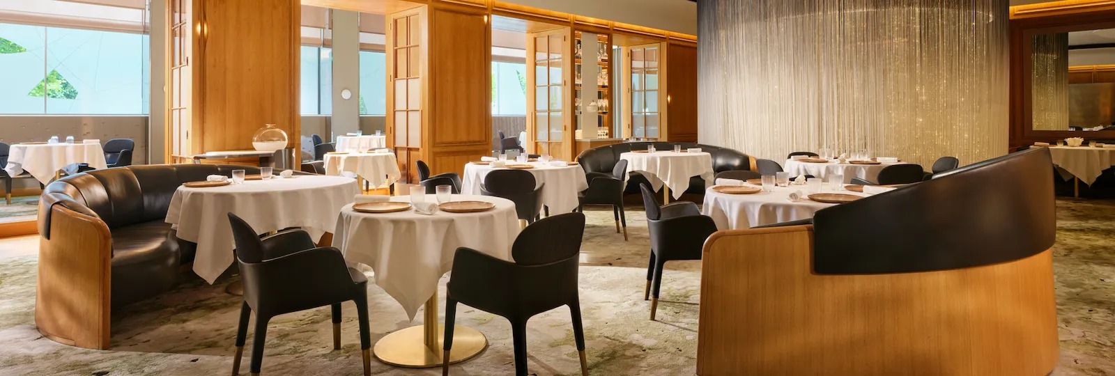 Elegant dining room at Alain Ducasse at The Dorchester featuring round tables dressed in white linens, contemporary seating, and warm wood-panelled interiors.