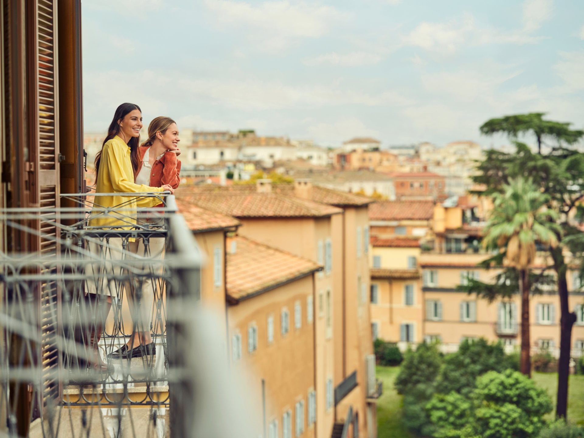 Two people enjoying a view from a balcony overlooking a cityscape on a bright day
