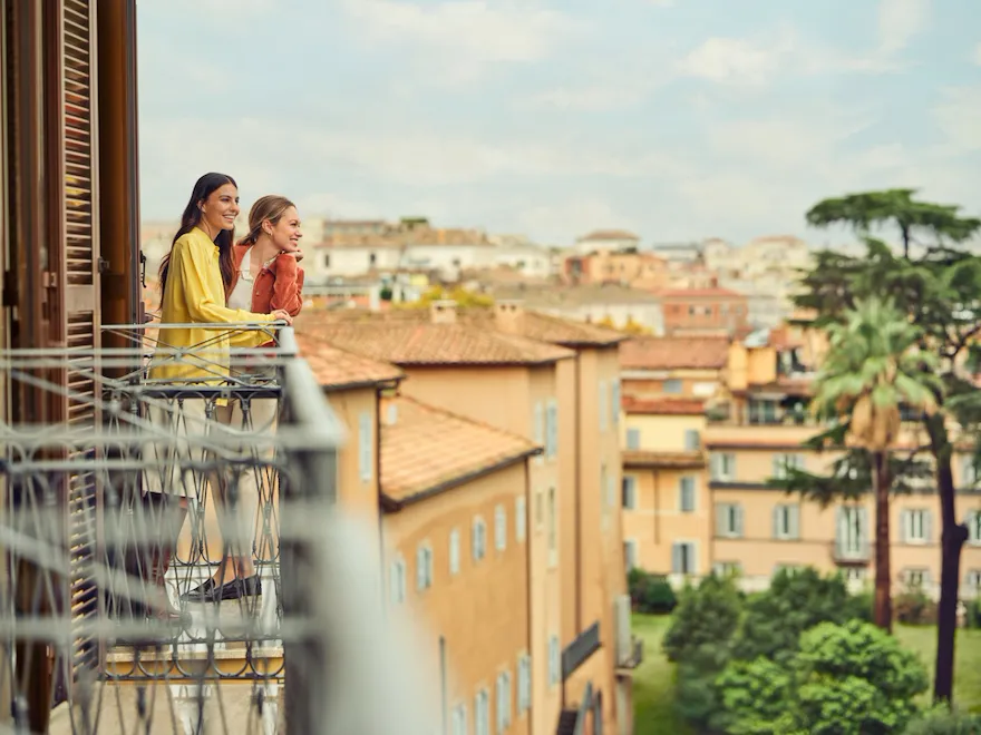 Two people enjoying a view from a balcony overlooking a cityscape on a bright day