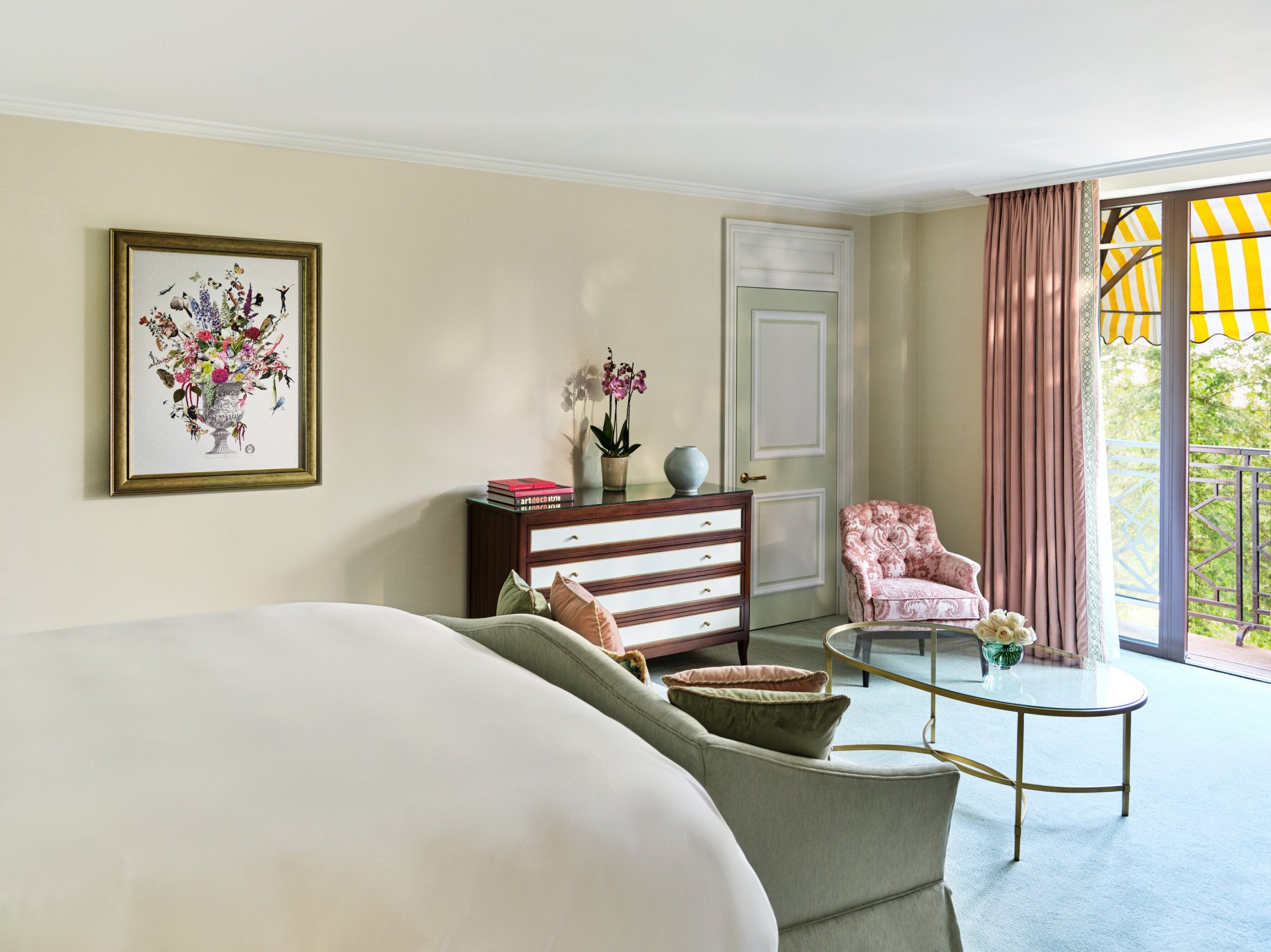 The Executive Park View Room at The Dorchester, showcasing a comfortable seating area with a pink floral armchair, glass coffee table, bespoke chest of drawers and French doors leading to a private balcony beneath the hotel's signature yellow-striped awnings.