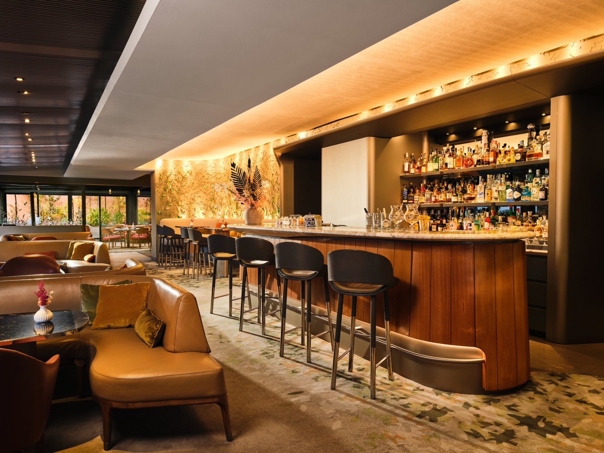 A modern bar with a seating area, illuminated counter, cozy atmosphere, and large windows.