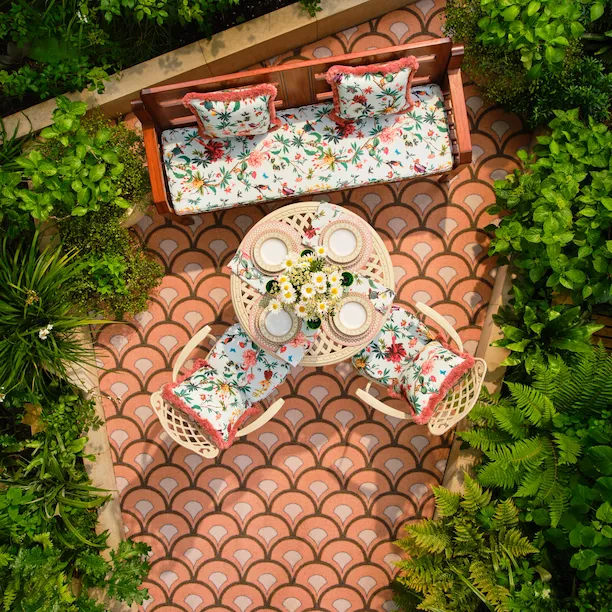 An overhead view of the La DoubleJ Summer Garden at The Dorchester, featuring colourful floral seating and a table setting surrounded by lush greenery.