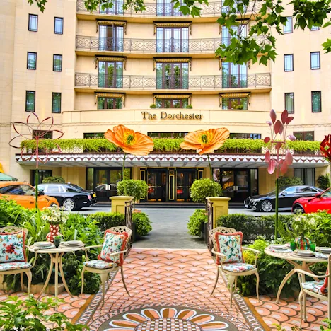 The La DoubleJ Summer Garden at The Dorchester, with colourful patterned seating, vibrant floral décor and views of the hotel entrance.