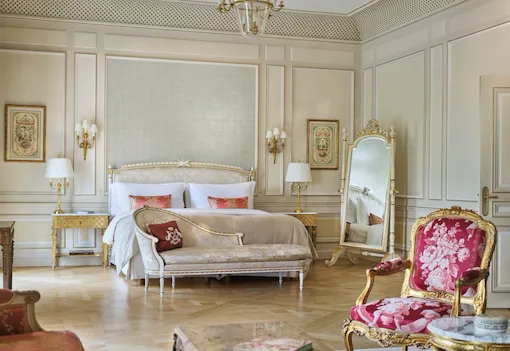 Large view of a Versailles Suite with the chair and the table in first plan and the couch, the bed and the mirror in the background, at Le Meurice, Paris
