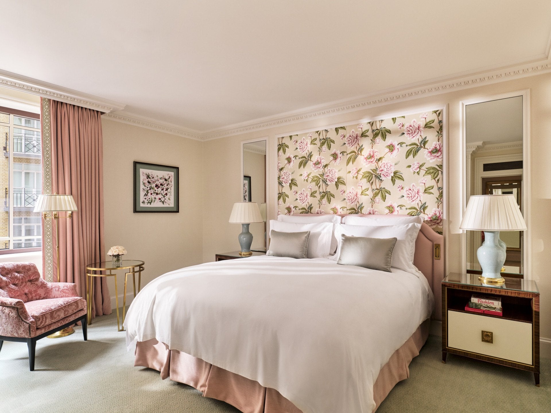 The Superior Room at The Dorchester, showcasing a king-sized bed framed by botanical floral wall coverings, blush-pink upholstery, classic bedside tables and soft natural light from the window.