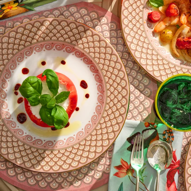 La DoubleJ Summer Garden tablescape featuring layered decorative plates, fresh seasonal dishes, green glassware, and floral accents in a vibrant celebration of outdoor dining.