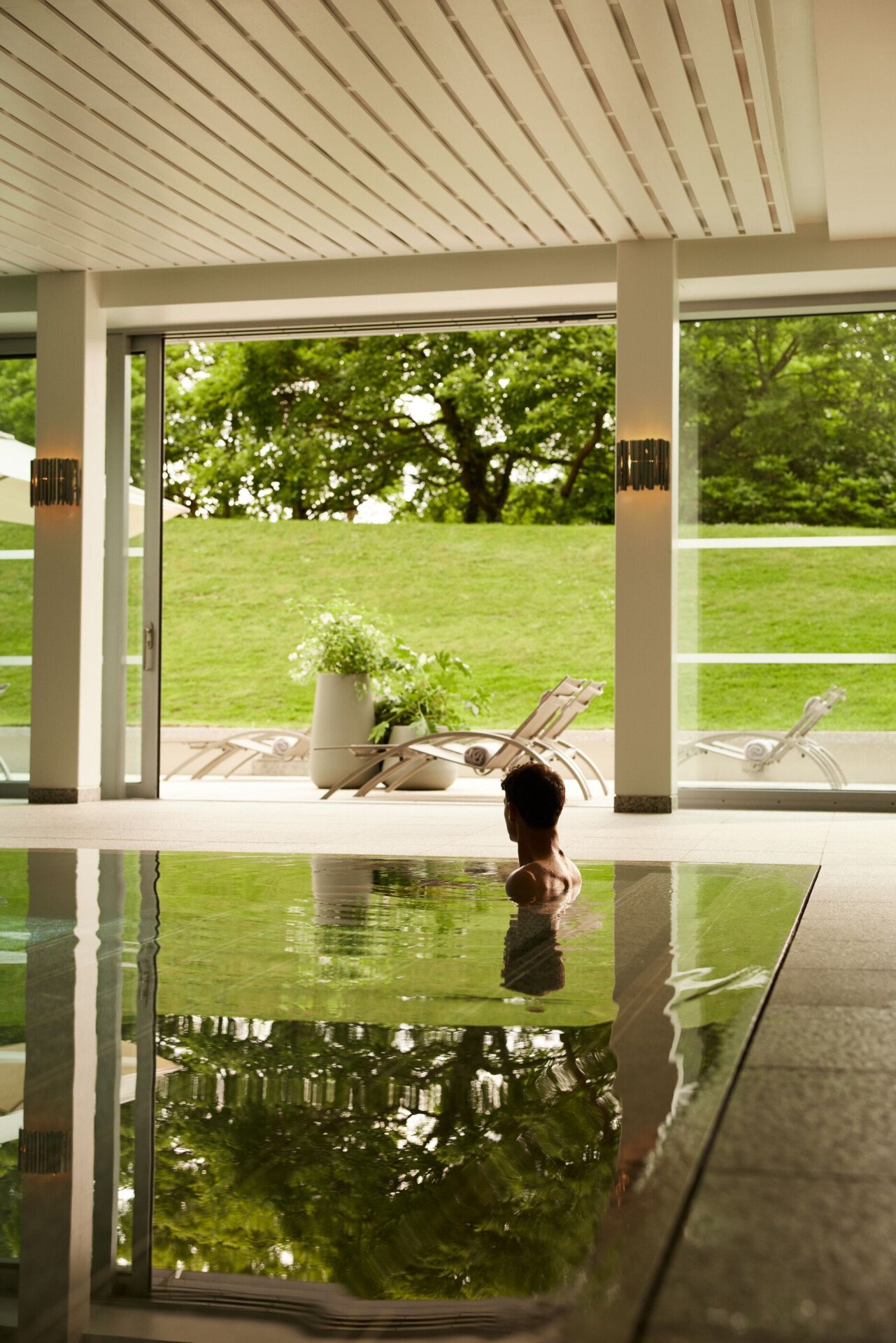 Guests enjoying the pool at Coworth Park with beautfiul light flooding through the open doors to the lush green forest and hills 