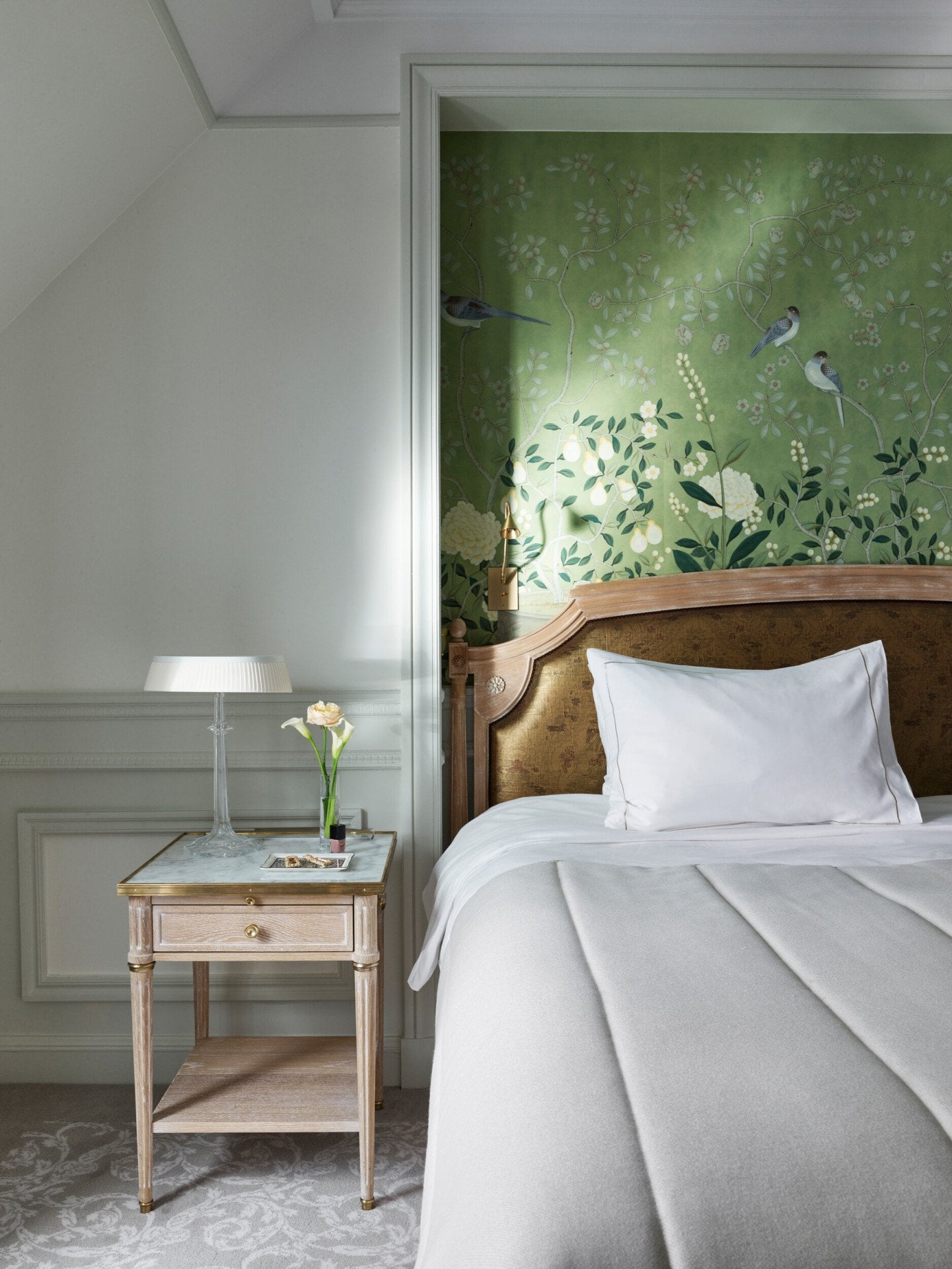 Portrait shot of an executive room with a green hand painted wall, and a wooden side table with a marble top. At Le Meurice, Paris.