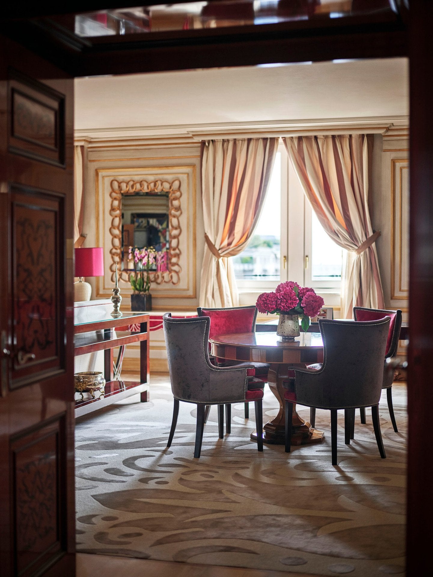 Executive Suite Living Room furnished with a wooden table, four red velvet chairs and a bouquet of pink flowers