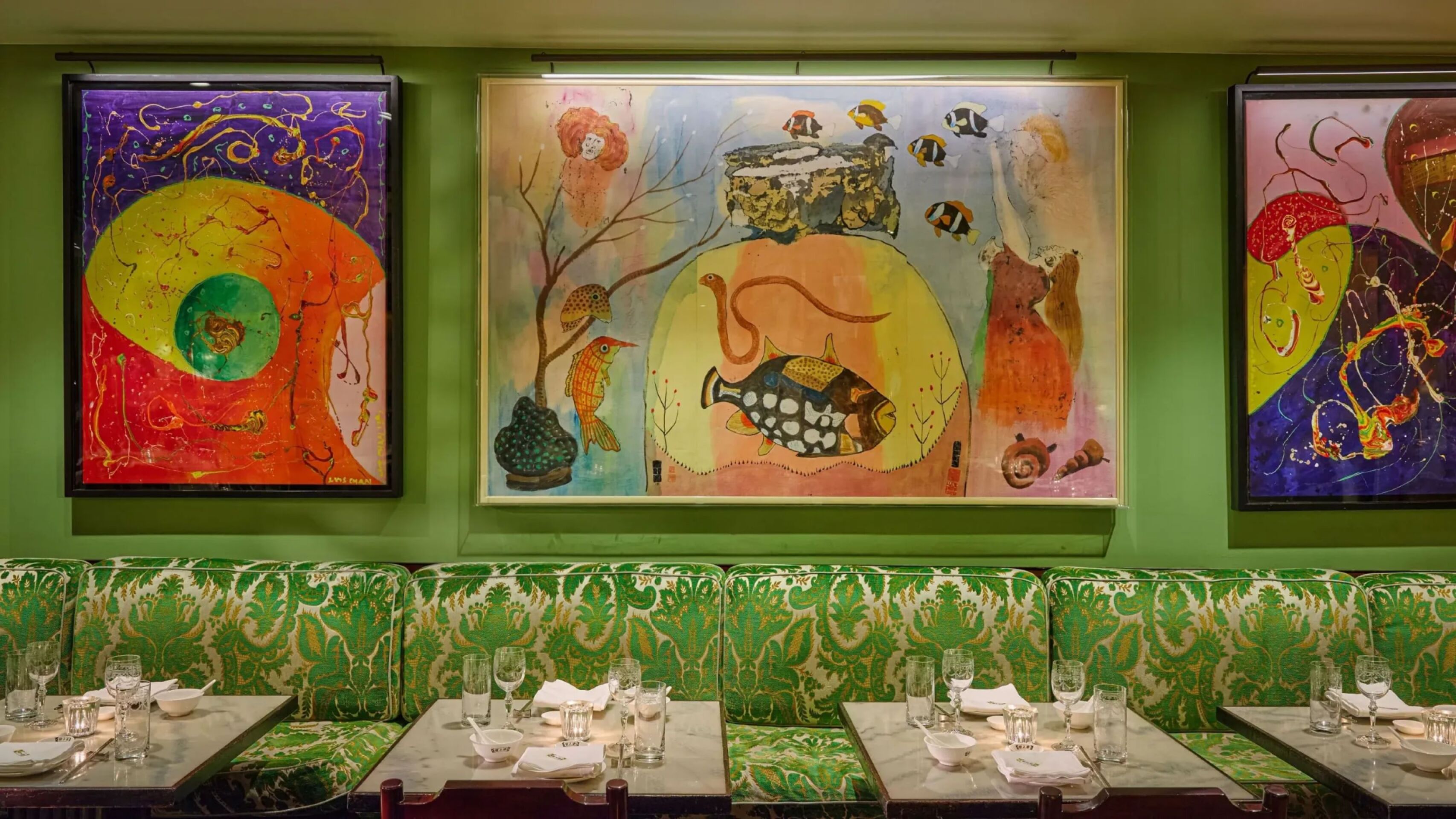Interior dining space at China Tang at The Dorchester, showcasing colourful contemporary artworks displayed against green walls, patterned upholstered banquette seating and tables set with fine tableware and glassware.
