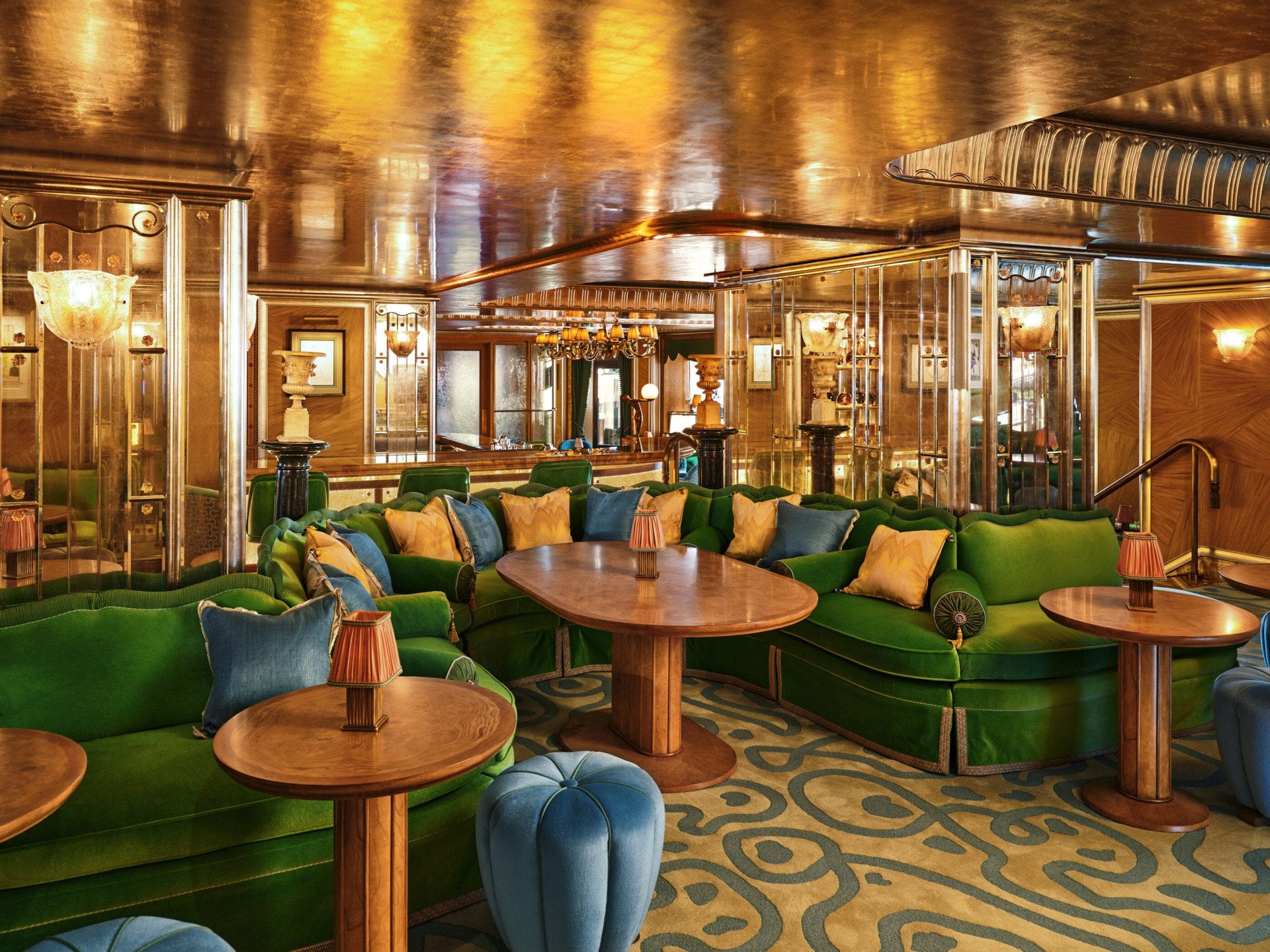 Curved green banquette seating and wooden tables at The Vesper Bar, set within warm Art Deco interiors.