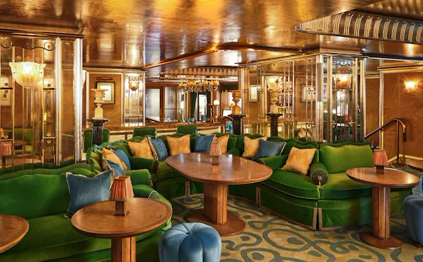 Curved green banquette seating and wooden tables at The Vesper Bar, set within warm Art Deco interiors.