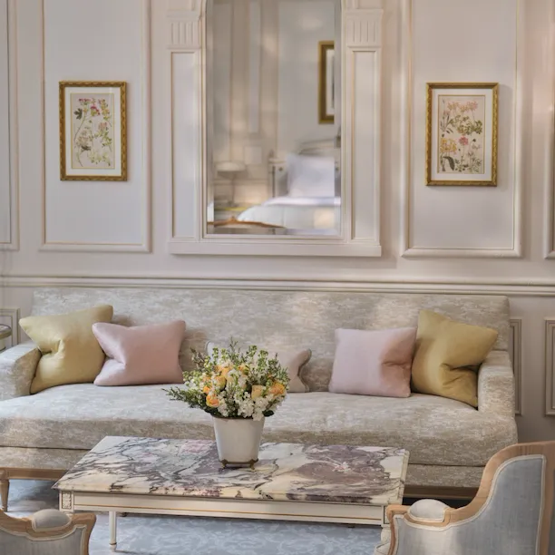 Livingroom area of a Deluxe Junior Suite with the table made with stone marquetry, the pillows on the couch and the mirror which reflect the bed, at Le Meurice, Paris
