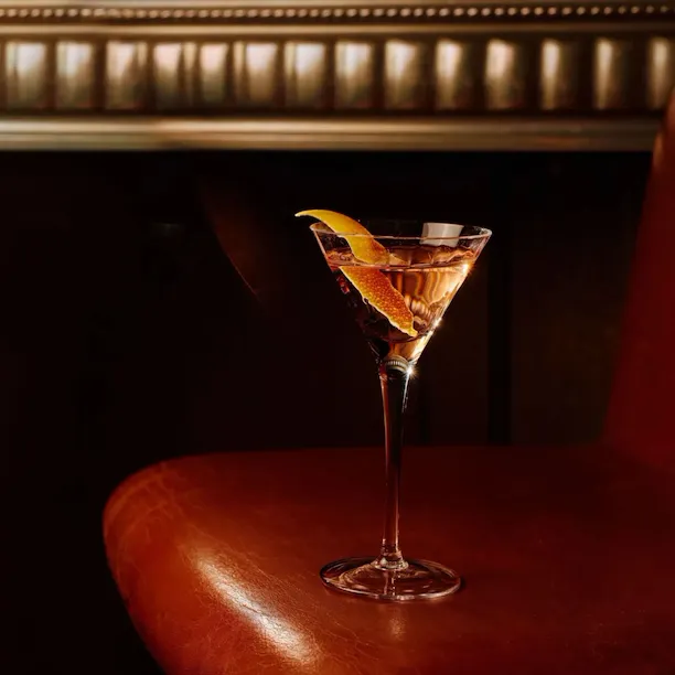 Signature Martini at The Grill at The Dorchester, elegantly presented in a classic stemmed glass and garnished with a lemon twist, set against the restaurant's warm leather seating and ambient lighting.