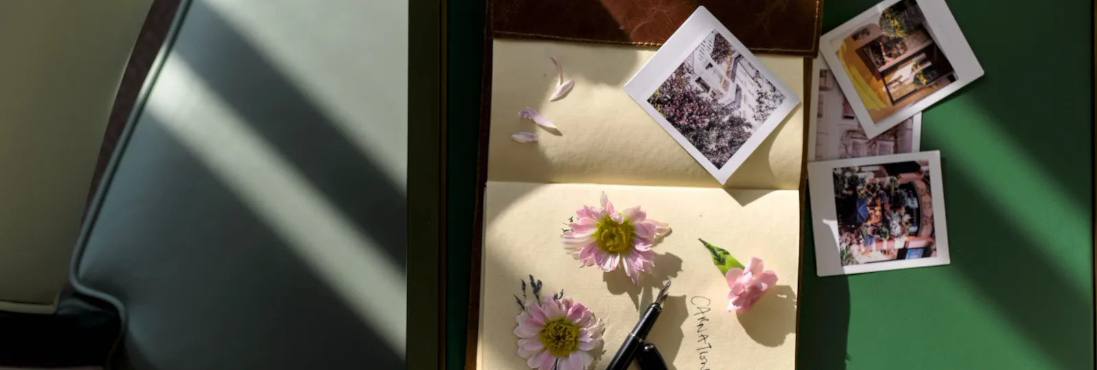Detail of the Executive Room at The Dorchester, showcasing a green writing desk with pressed botanical artwork, instant photographs, a pen and a bouquet of white roses illuminated by natural light.
