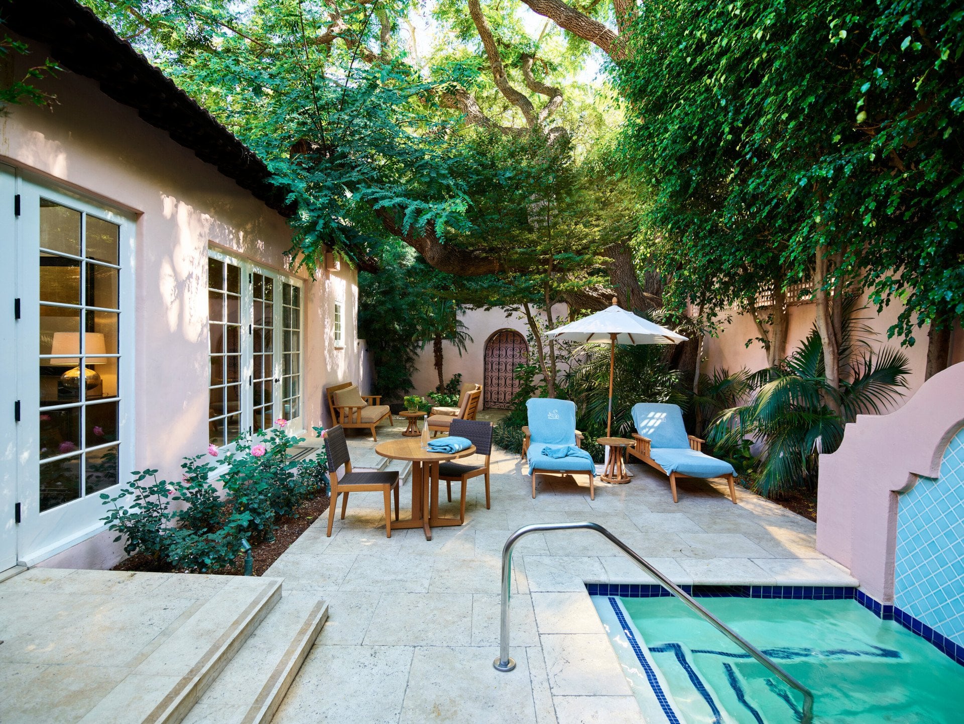 Spacious outdoor patio of the signature Grace Kelly Suite at Hotel Bel-Air with private plunge pool, two pool lounger with hotel-branded blue towels, an umbrella, a small dining table with two chairs, and additional patio furniture in the back of the patio.