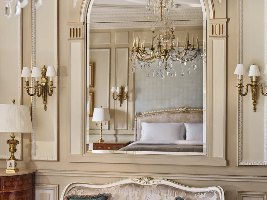 View on the table made with stone marquetry and a couch with a mirror above, which reflects the chandelier and the bed, at Le Meurice, Paris