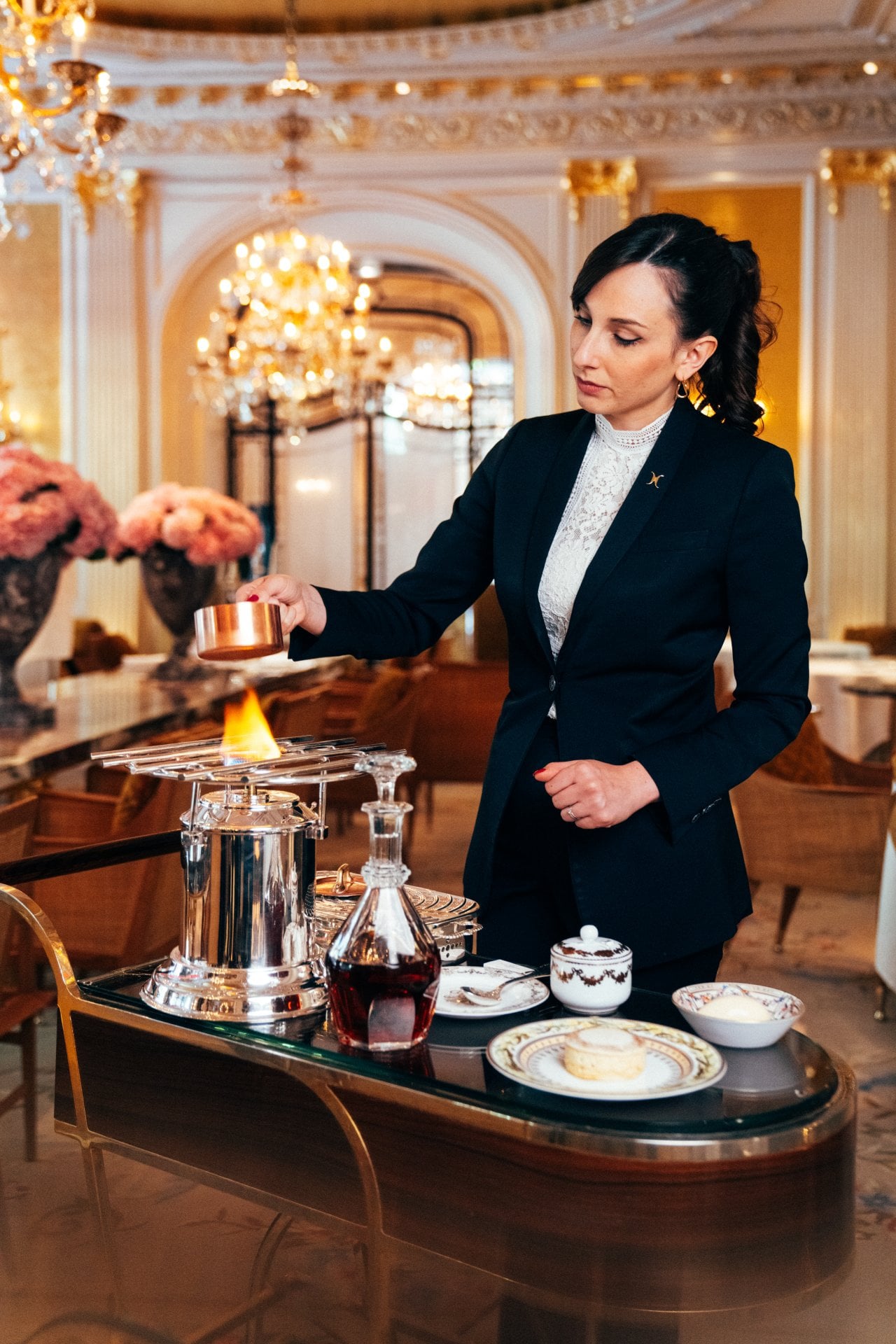 Person in formal attire conducts a flaming demonstration at a luxurious indoor setting.