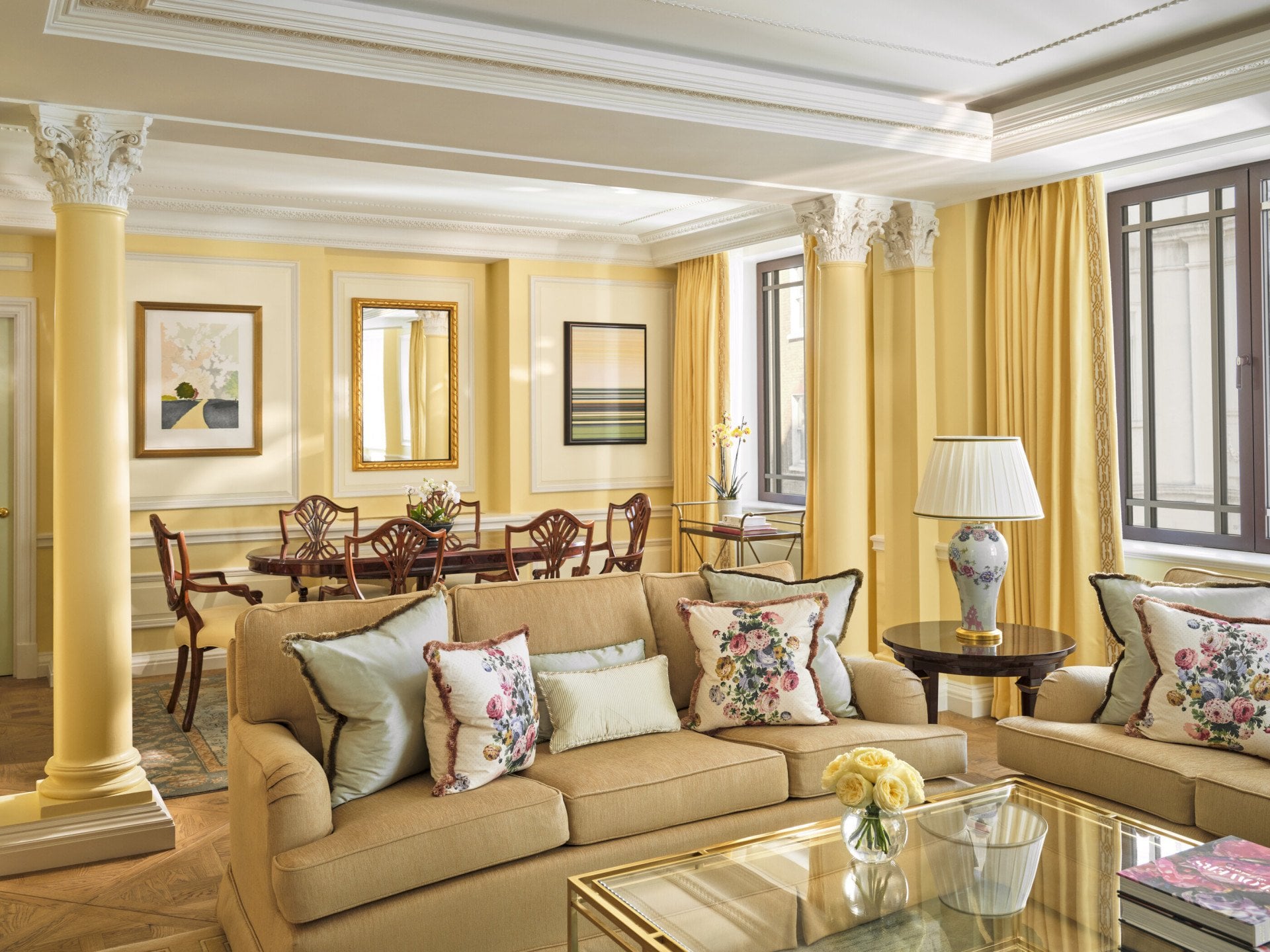The Dorchester Suite bathed in evening light, showcasing yellow walls, a wooden dining table and an expansive living room designed for comfort and elegance.