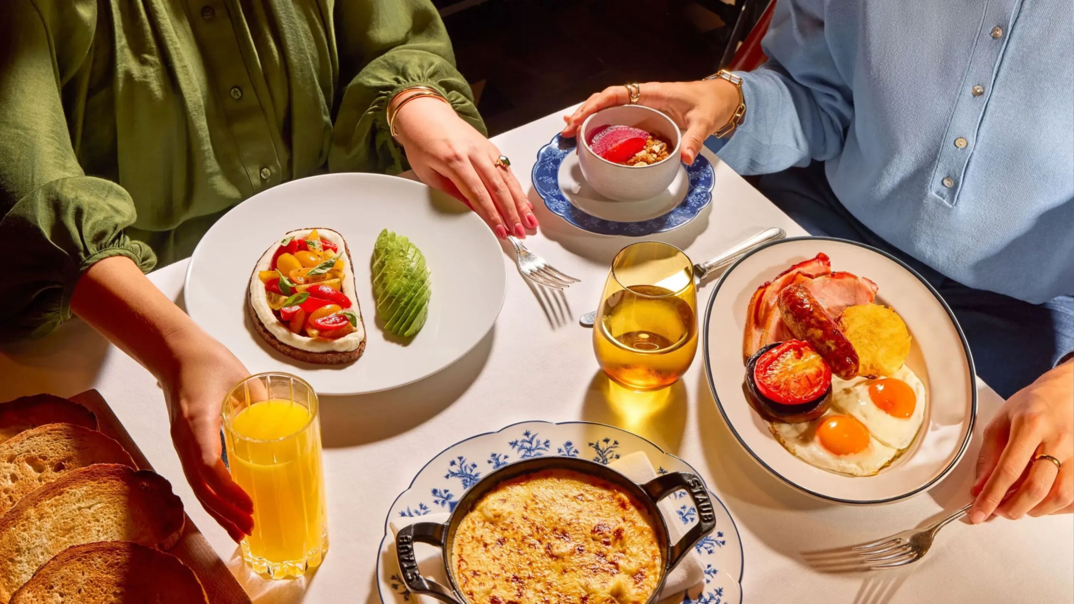 Dining table at The Grill at The Dorchester, showcasing a selection of breakfast and brunch dishes including tomato on toast with basil, eggs and bacon, a baked gratin-style dish, fresh berries and glasses of orange juice.