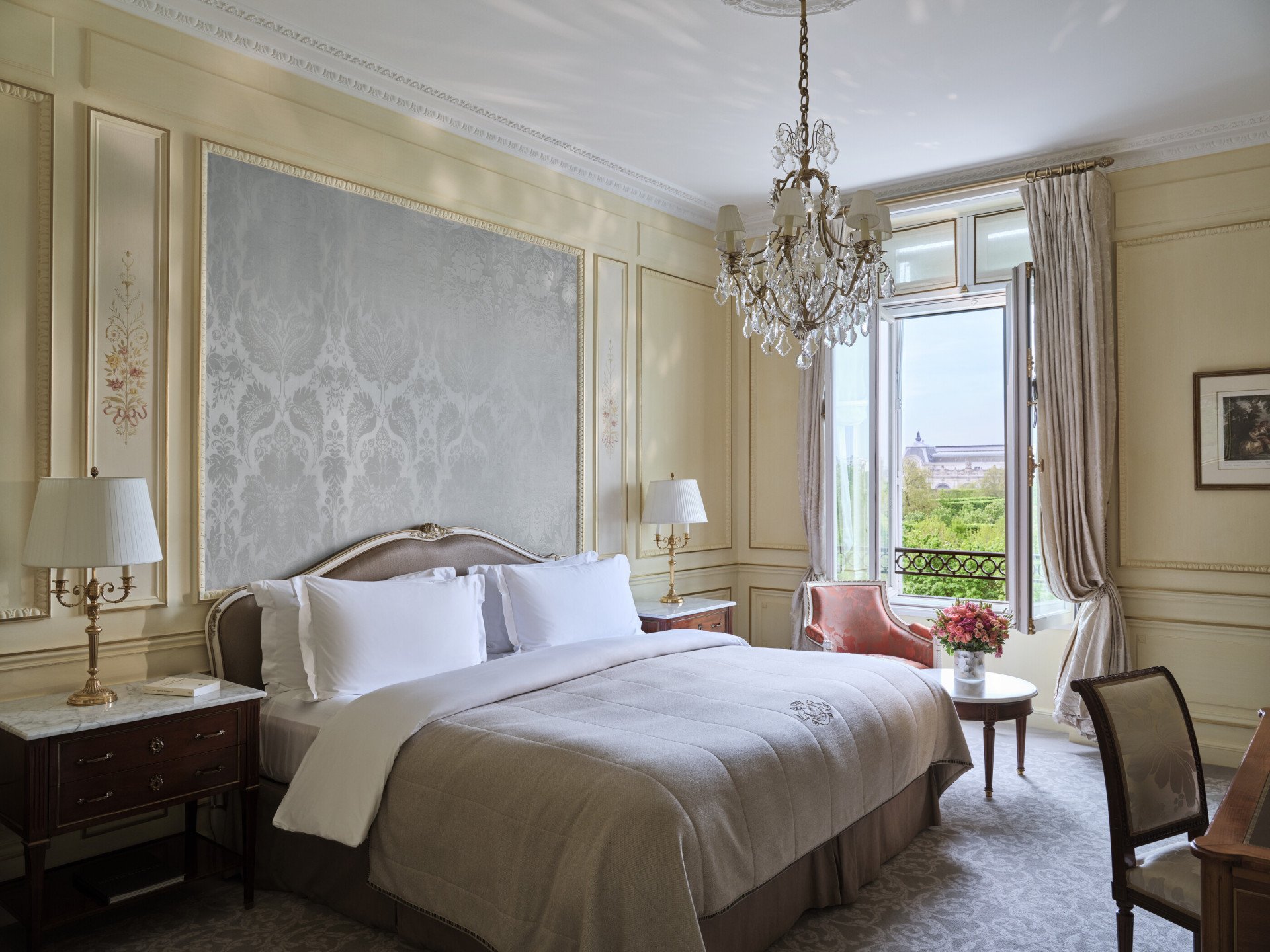 Heritage Suite view from the right side of the bed, next to a chair and a table with flower on the top, in front of the window, at Le Meurice, Paris