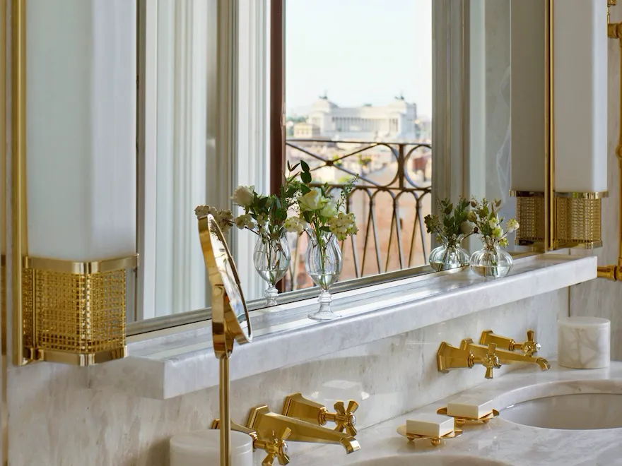 White marble bathroom with double sinks and view of Vittoriano reflected in mirror inside Presidential Suite at Hotel Eden, Rome